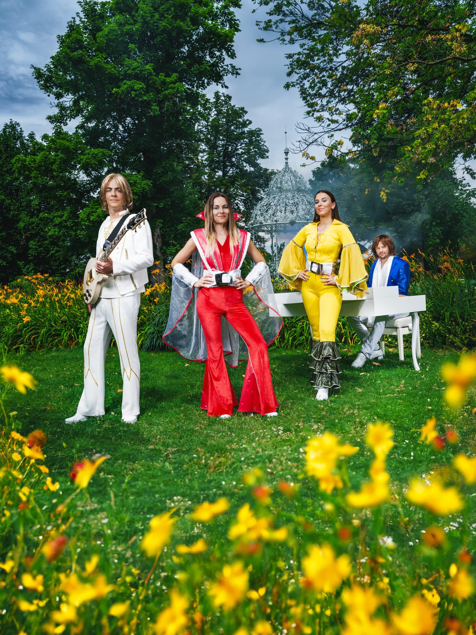 Band in gelb/rot/blau/weiß auf einer Blumenwiese vor einem Pavillon, Sommerlicht